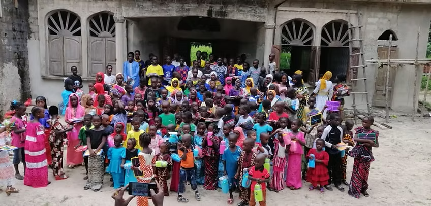 Large group posing in front of a stone building, wearing colorful clothes and facing the camera
