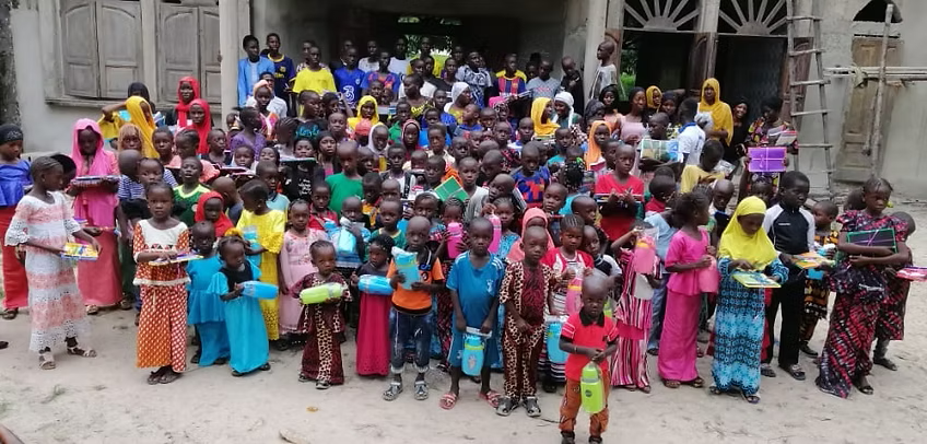 Large group gathered outside a building, many holding plates and wearing colorful clothing, posing for a photo