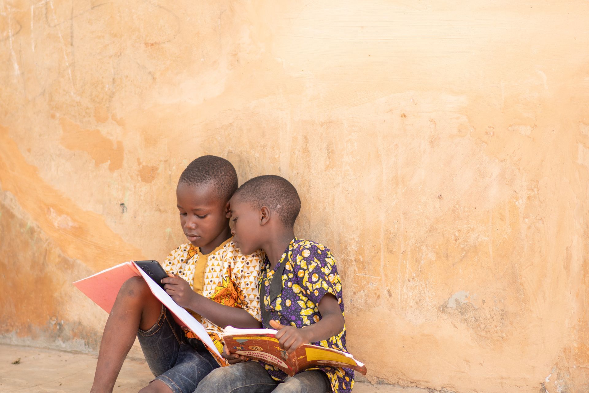 Two children reading a book together against a tan wall