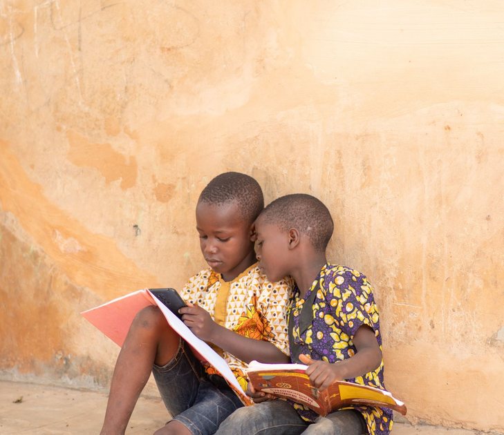 Smiling child writing in a notebook at a desk with a laptop nearby