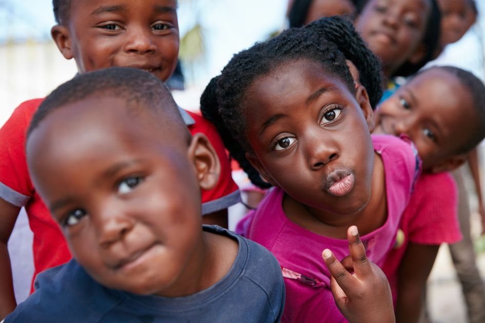 Children posing playfully for the camera, two in front with curious expressions and bright shirts