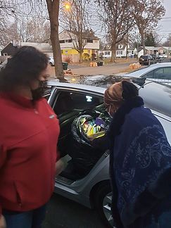 Two people loading a colorful bag into a car on a suburban street at dusk