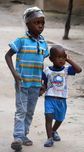 Two children walking outdoors, one in a blue plaid shirt and the other in a blue T-shirt.