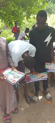 People browsing colorful books at an outdoor market stall under trees