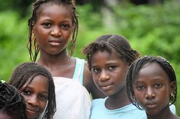 Four children standing outdoors, looking at the camera in a green setting.