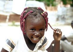 Smiling child with pink braided hair, holding a braid outdoors.