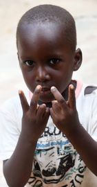 Child in a white shirt making a hand gesture with fingers raised near the face