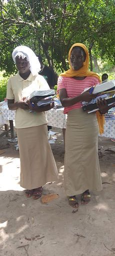 Two people outdoors holding folded black clothing, one in a white headscarf and one in a yellow veil.