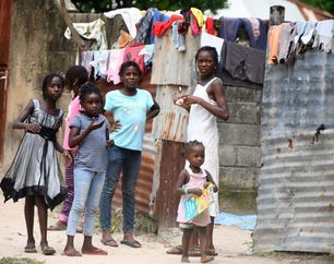 Five people stand by a corrugated metal wall with laundry hanging overhead.