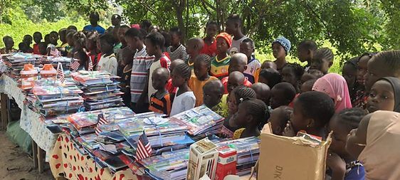 Crowd gathered around stacks of donated supplies outdoors under trees