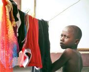 Child beside hanging colorful clothes, looking at the camera indoors.