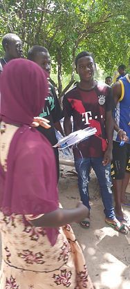 People gathered outdoors in a shaded area, one person holding papers while others listen.