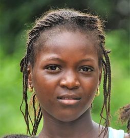Portrait of a person with braided hair, neutral expression, against a blurred green outdoor background