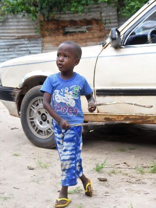 Child walking past a parked white car, wearing a blue shirt and blue tie-dye pants.
