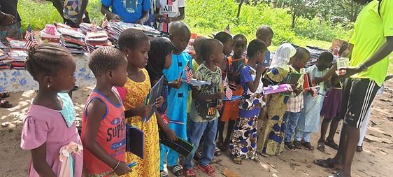 Children standing in a line outdoors, holding small items and cups during a community gathering