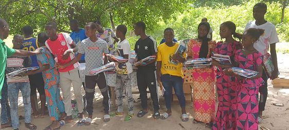 Group of people standing outdoors, reading papers and holding items in a leafy area