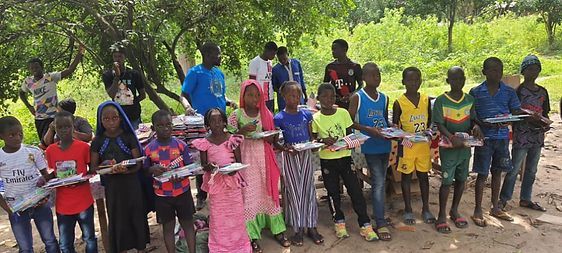 A group of children standing outdoors, holding colorful items under trees.