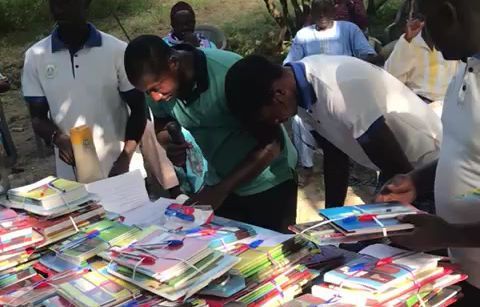 People browsing piles of colorful books at an outdoor table.