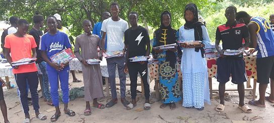A group of people stand outdoors holding colorful items, with trees and dirt ground in the background.