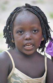 Close-up of a child with braided hair wearing a light-colored dress, looking at the camera.
