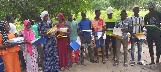 People standing outdoors in a line, holding folders and papers, in a tree-lined area.