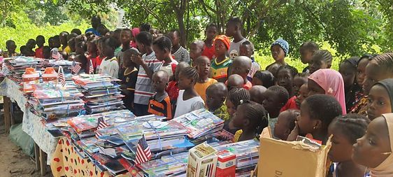 Crowd gathered outdoors around stacks of donated supplies on tables under trees