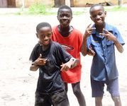 Three children posing and smiling outdoors, wearing black, red, and blue shirts.