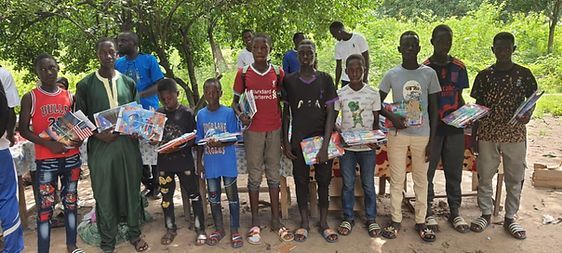 Group of people standing outdoors in a line, holding items and posing in bright daylight.