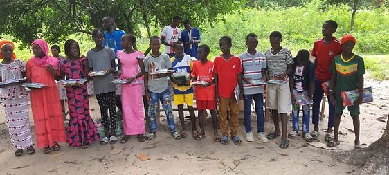 Group of children standing outdoors on a dirt path, posing together in colorful clothing with trees behind them