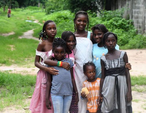 Group of six children standing together outdoors on a grassy path, smiling at the camera.