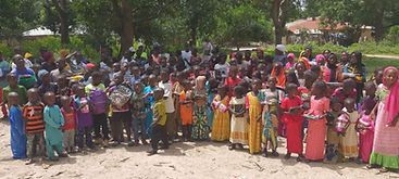 Crowd gathered outdoors with many people in colorful clothing in a tree-lined area