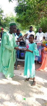 People in mint-green outfits at an outdoor gathering, with a child standing in front holding a tray.