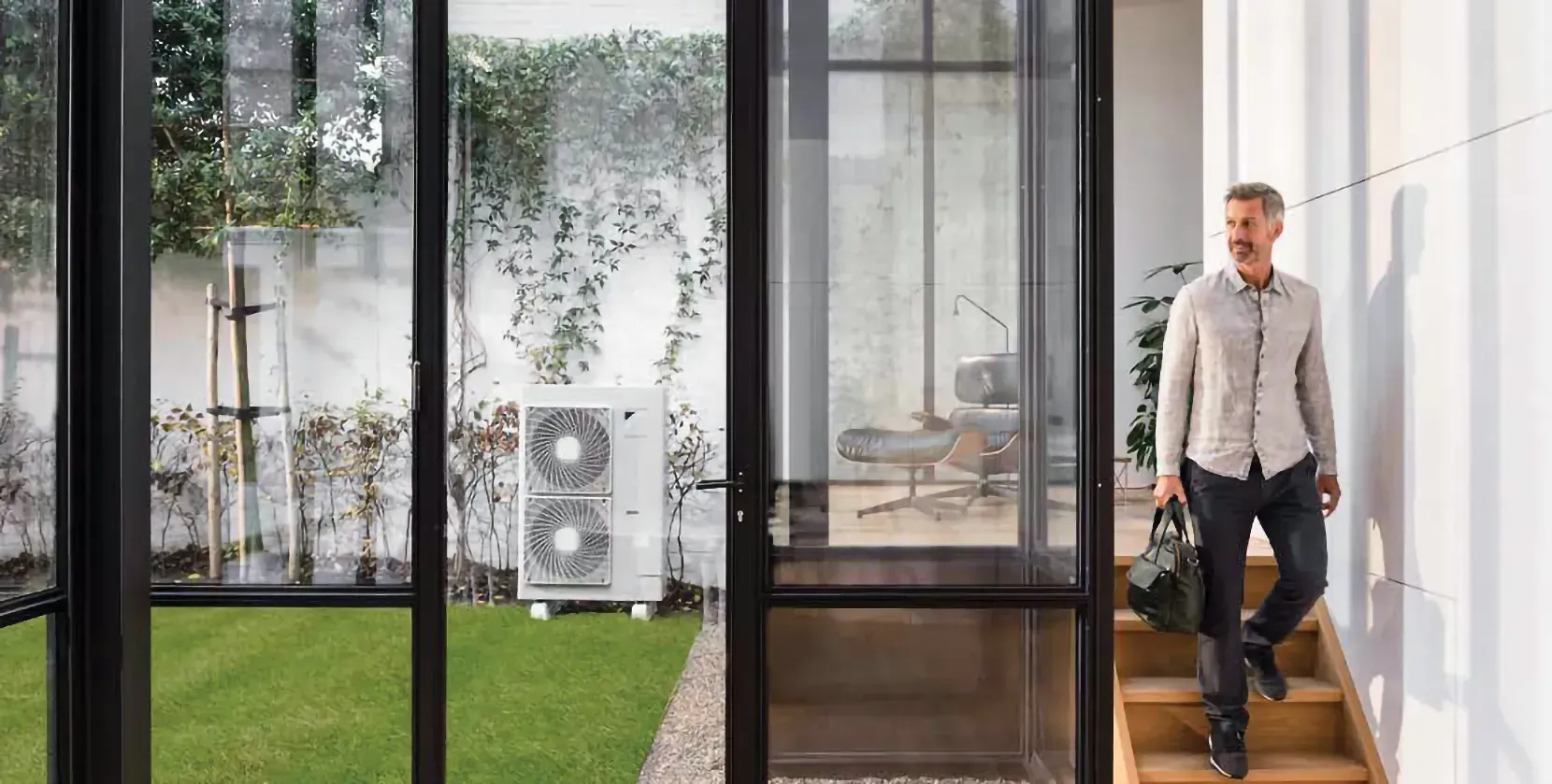 Man walking down stairs into a room with a view of a yard and HVAC unit.