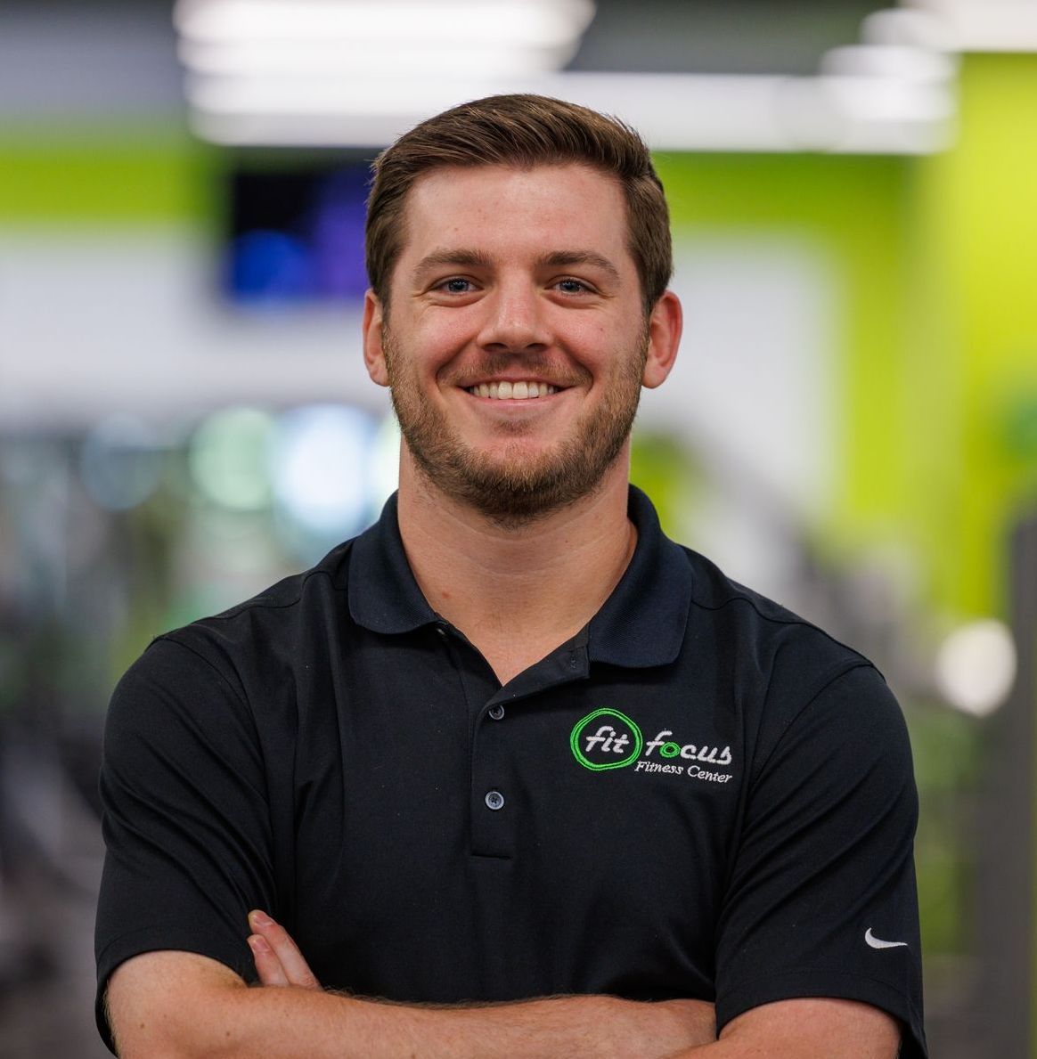 Man with arms crossed smiling, wearing a black polo shirt with