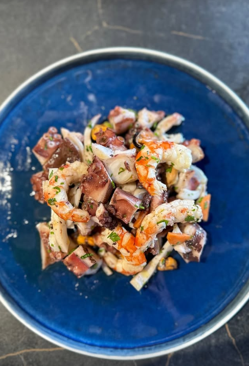 Insalata di mare con polpo e gamberi su un piatto blu.