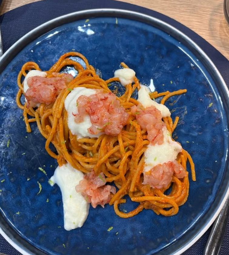 Spaghetti con salsa rossa, gamberi e salsa bianca su un piatto blu.