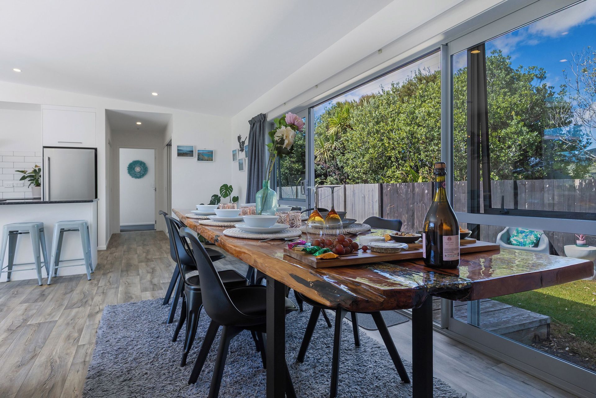 Dining room with long wooden table set for meal, overlooking a yard through a large window.
