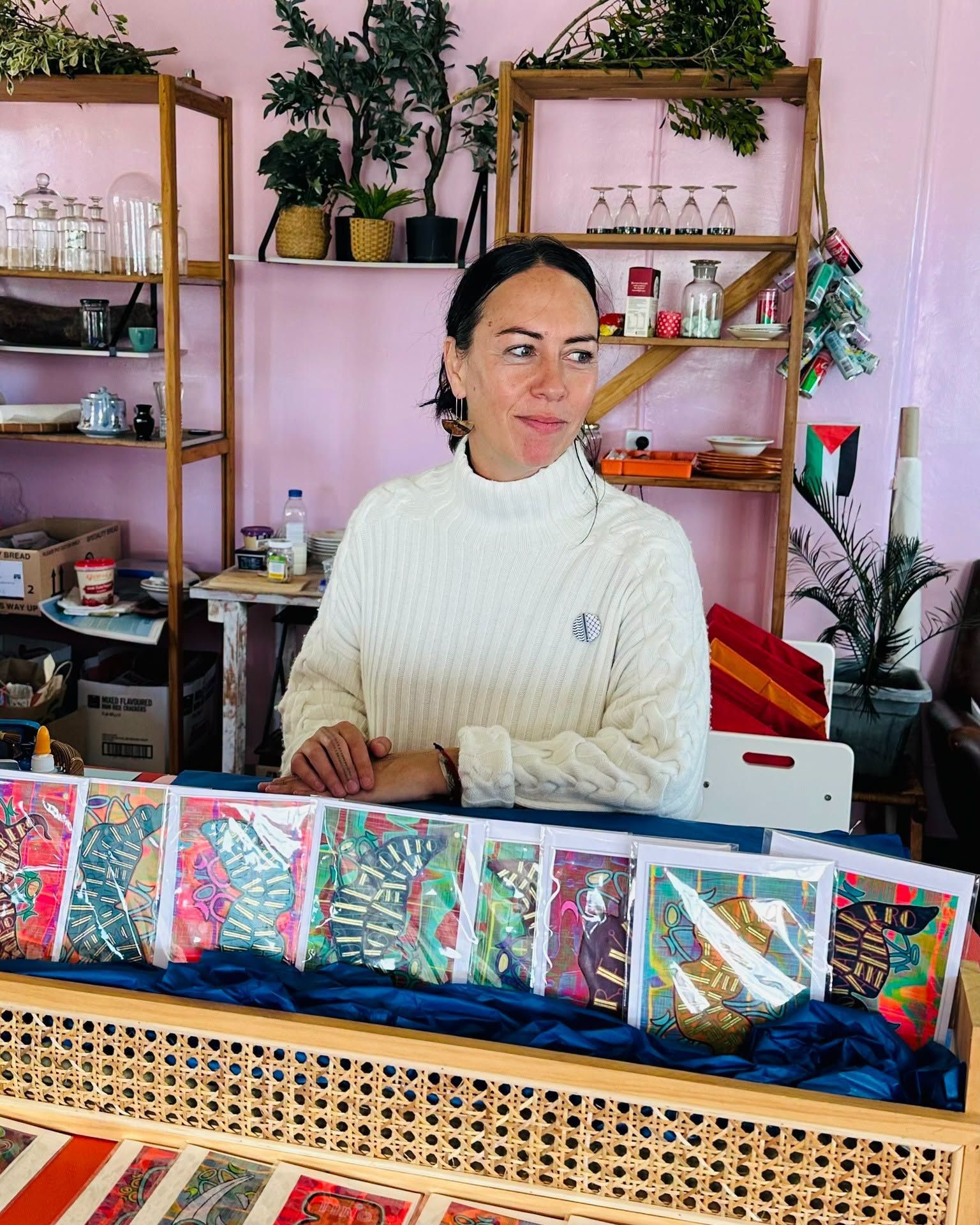 Woman in a white sweater behind a woven display of colorful packaged goods in a shop-like room
