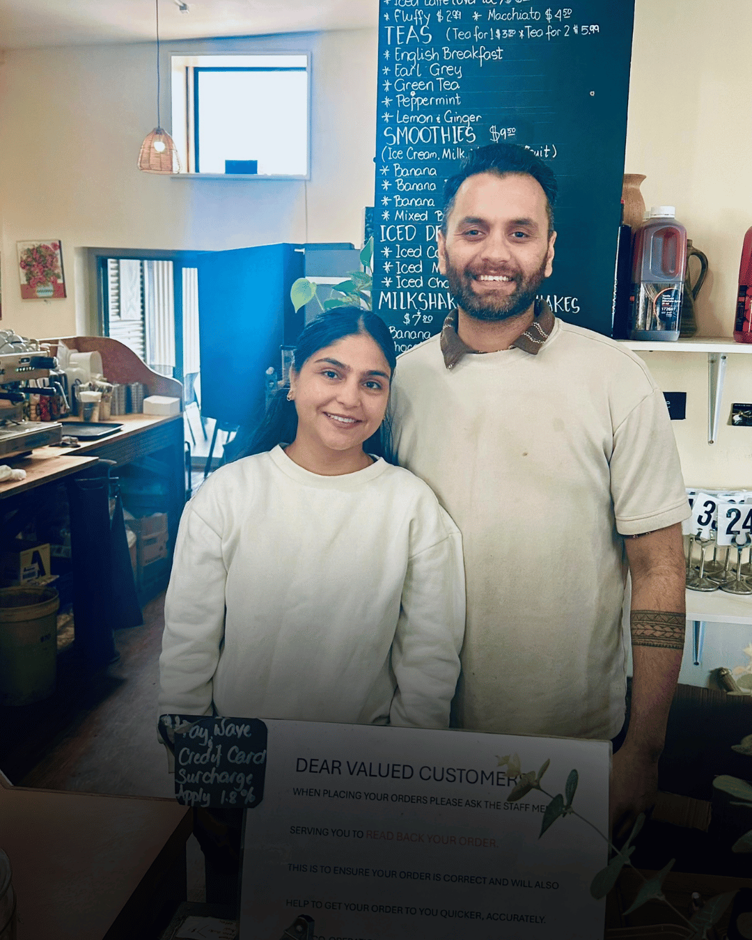 Two smiling café staff standing behind a counter with a menu board in the background