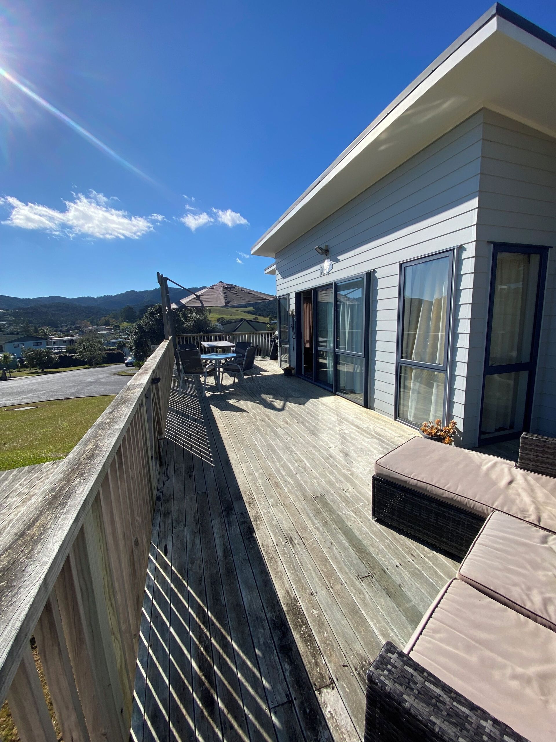 Wooden deck with house, sun, and mountain view. Blue sky.
