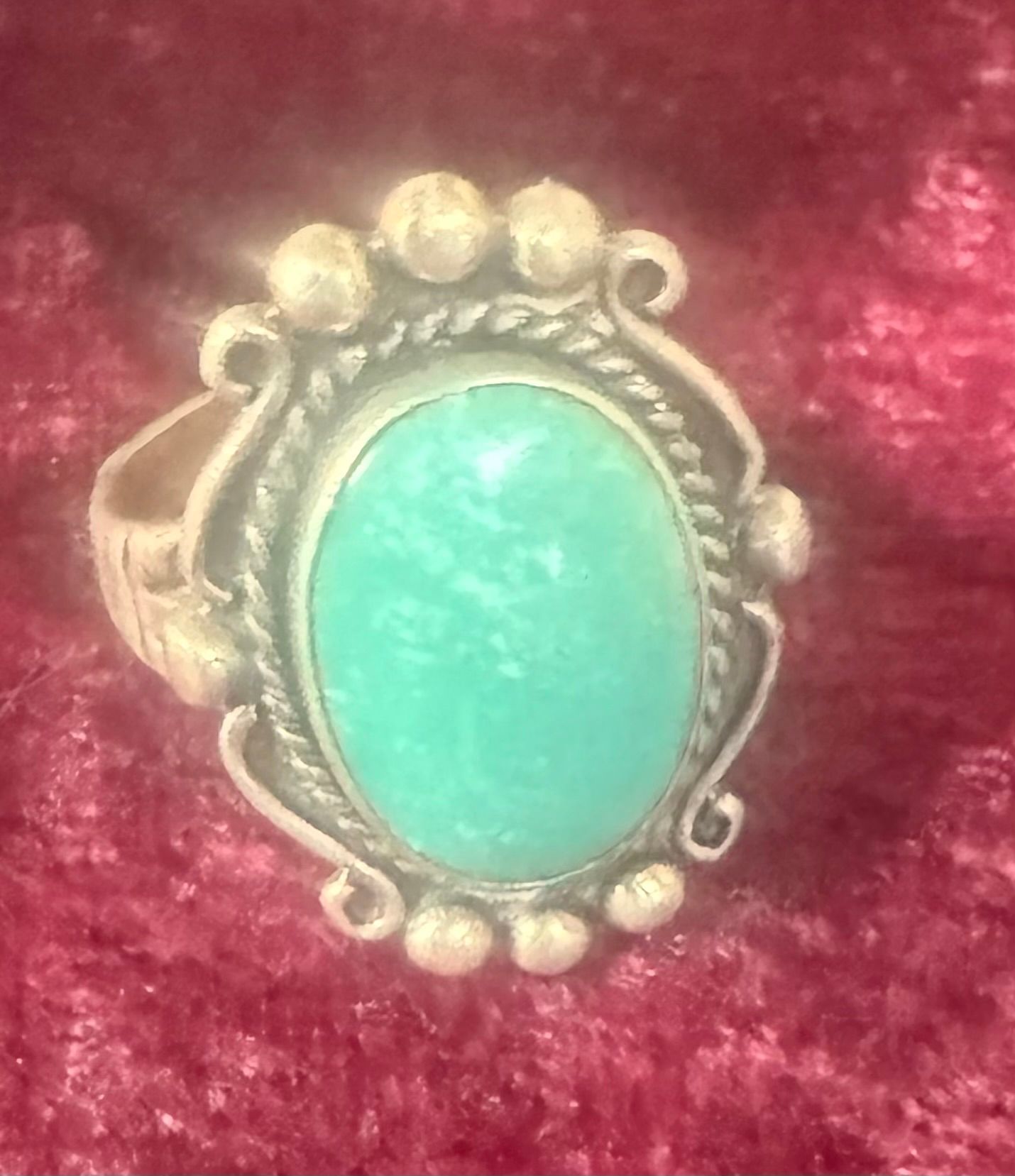 Oval green stone ring in a silver setting with small decorative beads, resting on red velvet.
