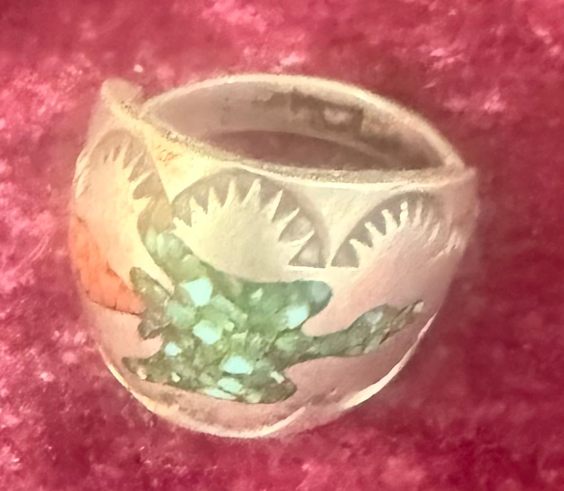 Silver ring with a green turtle design and etched leaf patterns on a pink fabric background