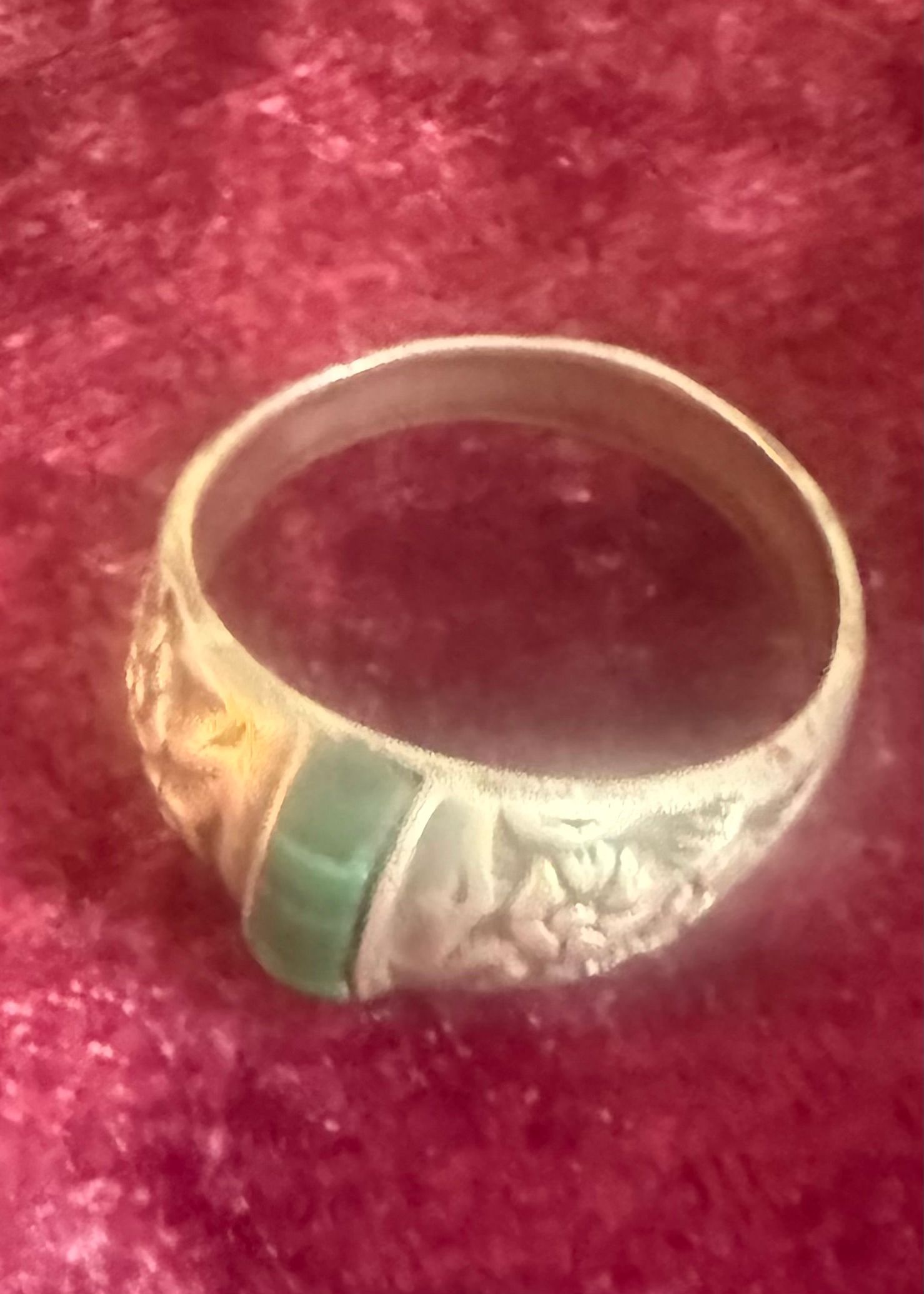 Gold ring with green and orange accents on a red velvet background
