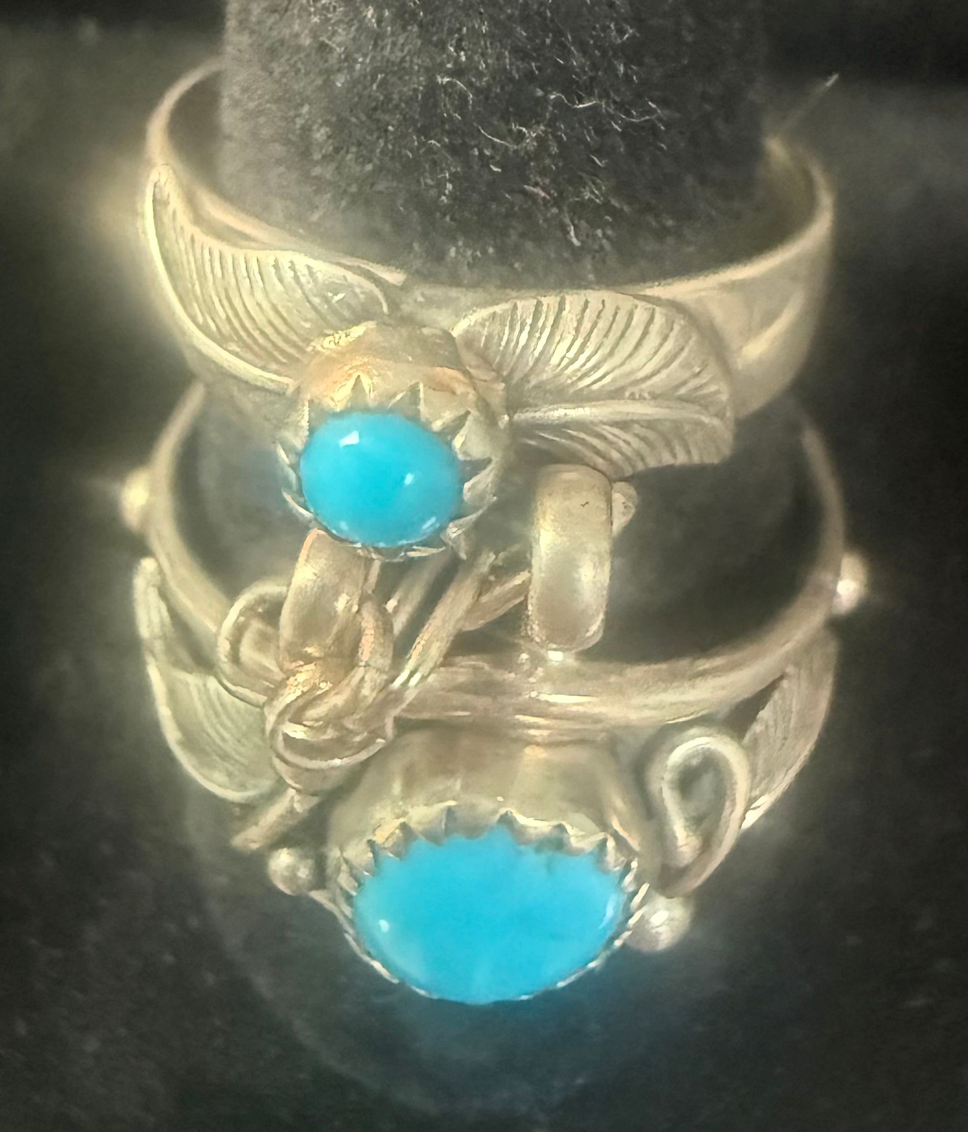 Two silver rings with turquoise stones on a finger, one with a winged design and floral detail.