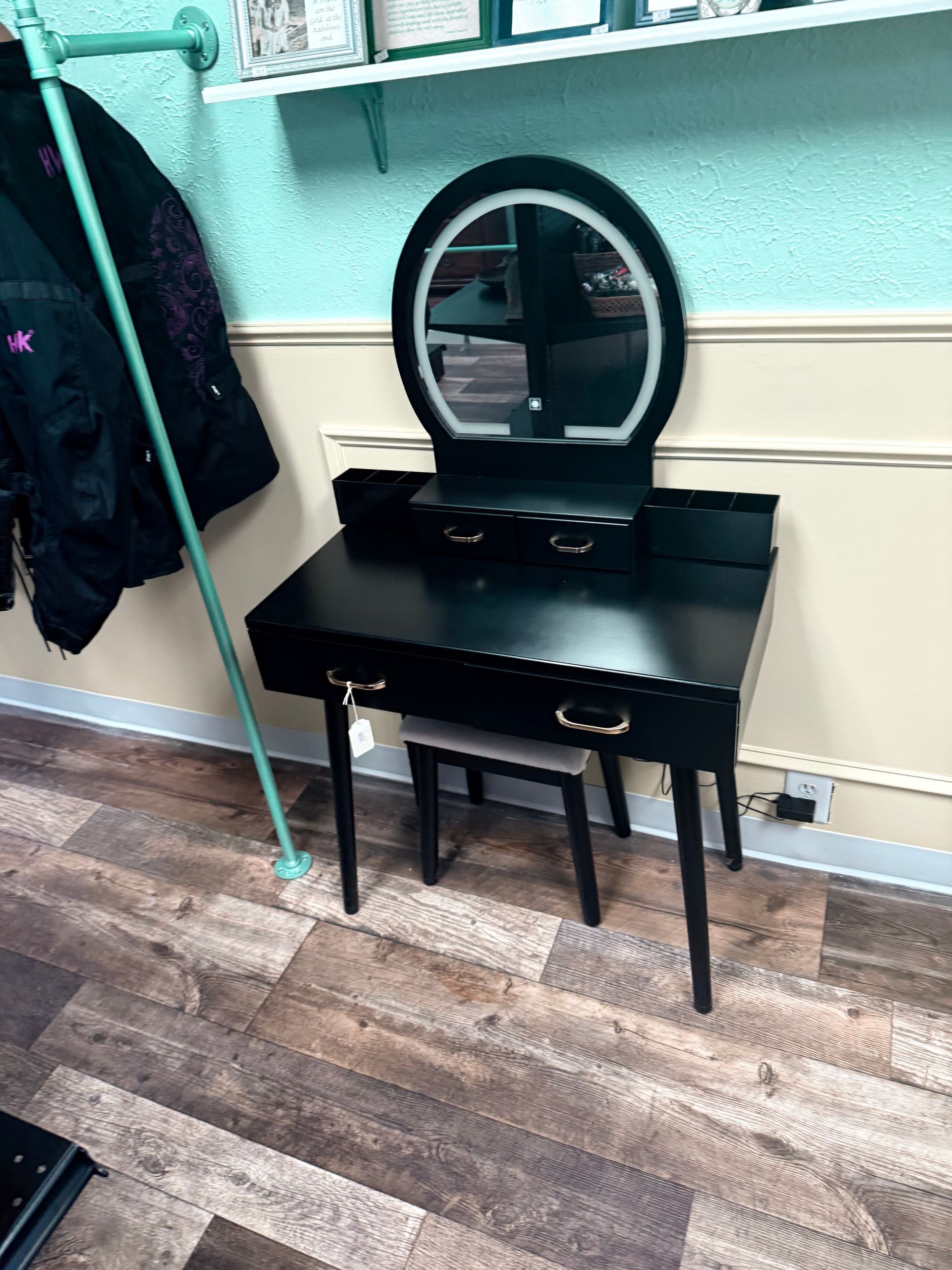 Black vanity table with round mirror and stool against a wall in a small room