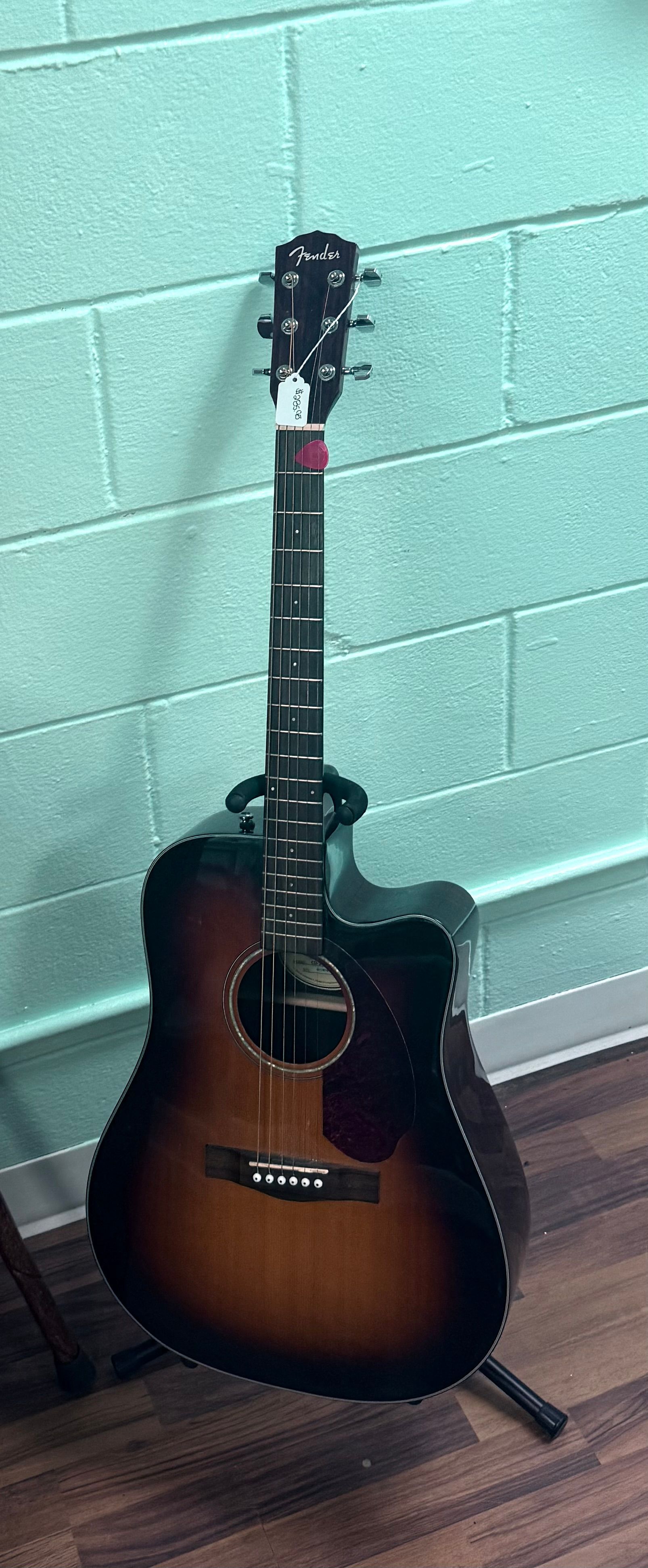 Acoustic guitar on a stand against a mint-green cinderblock wall.