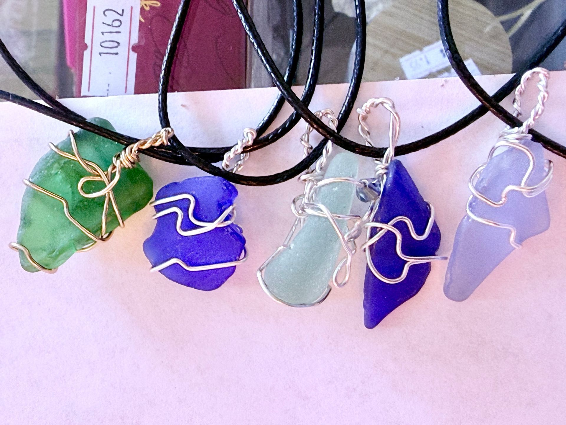Wire-wrapped sea glass pendants in green, purple, and blue on black cords