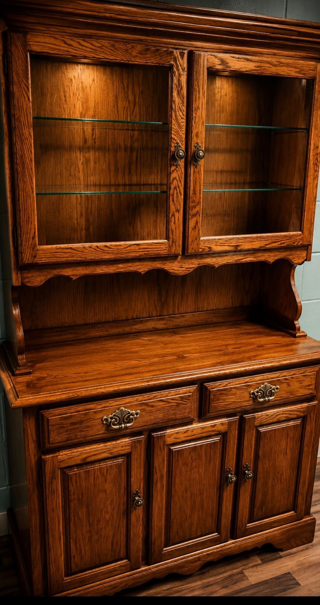 Dark wooden hutch and cabinet with glass-front upper doors and three lower drawers in a warm-lit room