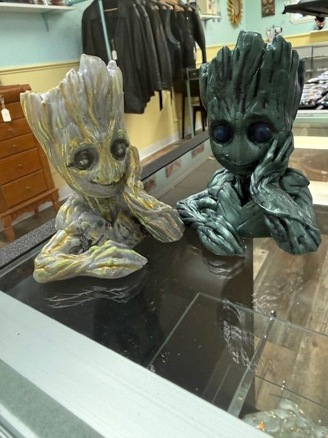 Two small Groot figurines on a table in a store, one gold and one dark green.