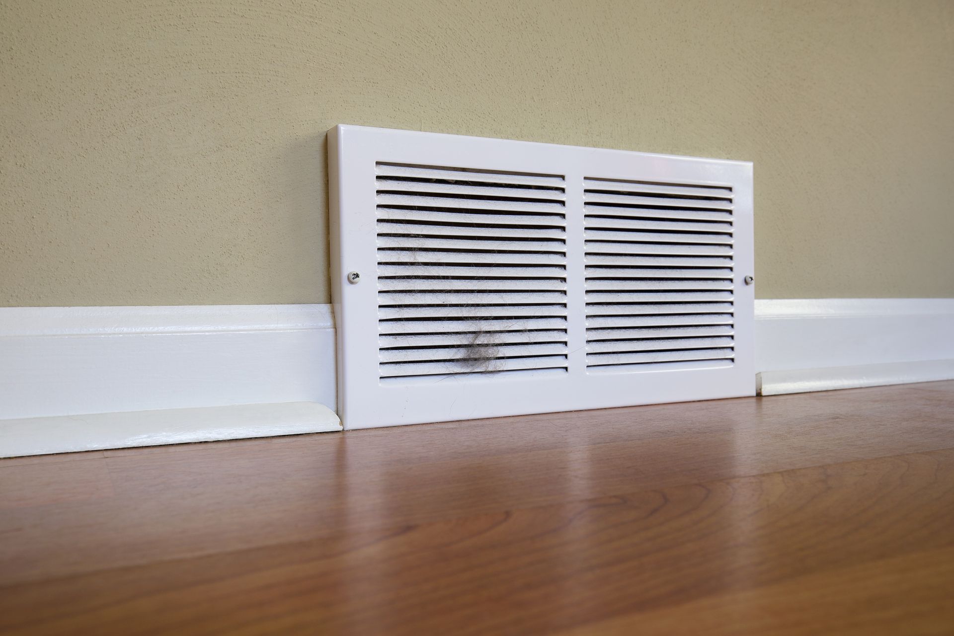 A white HVAC vent register on a wall with dark dust and debris visible between its slats